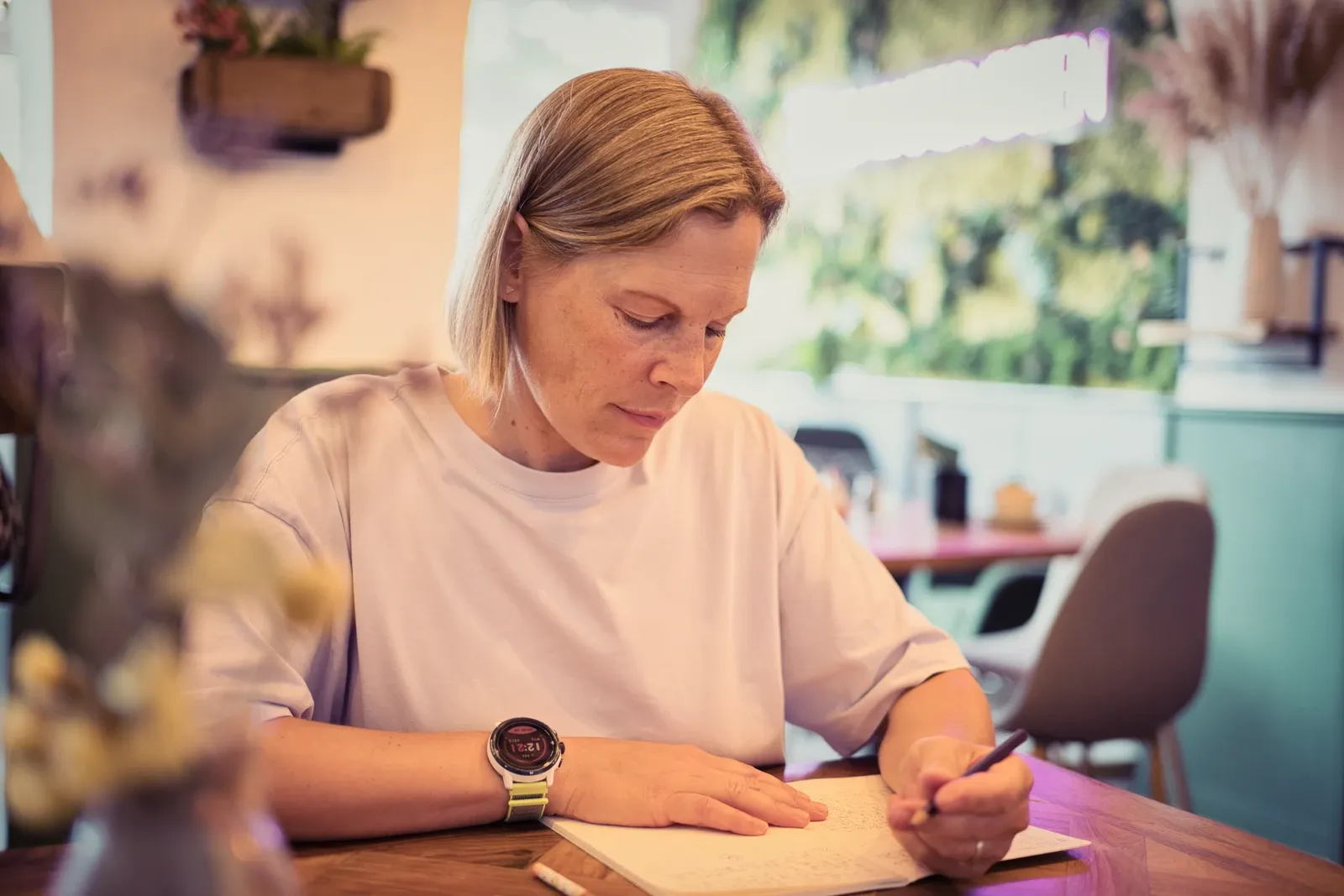 Die Autorin Peaches Keeley Anderson sitzt an einem Tisch und schreibt in ein Notizbuch. 